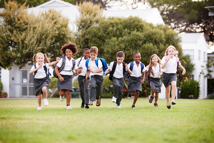 Group pf school children in school uniforms happily running across school field