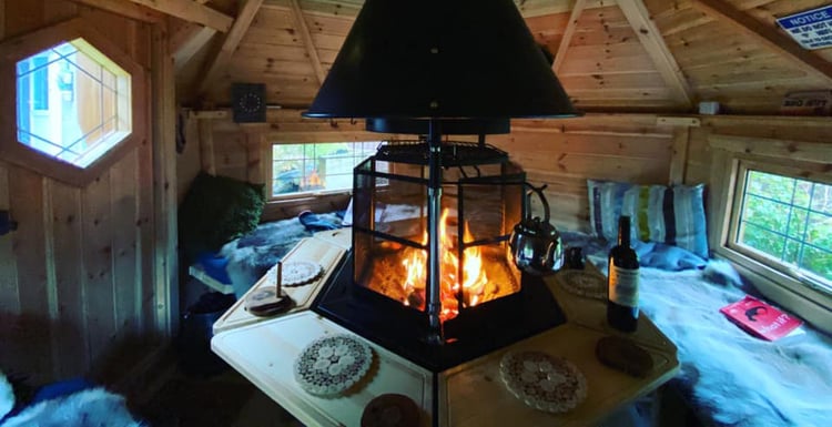Interior of a log forest cabin with fire lit and tall spark guard 
