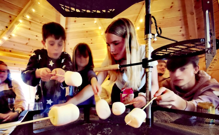 Children roasting marshmalllows over coals inside their forest school cabin